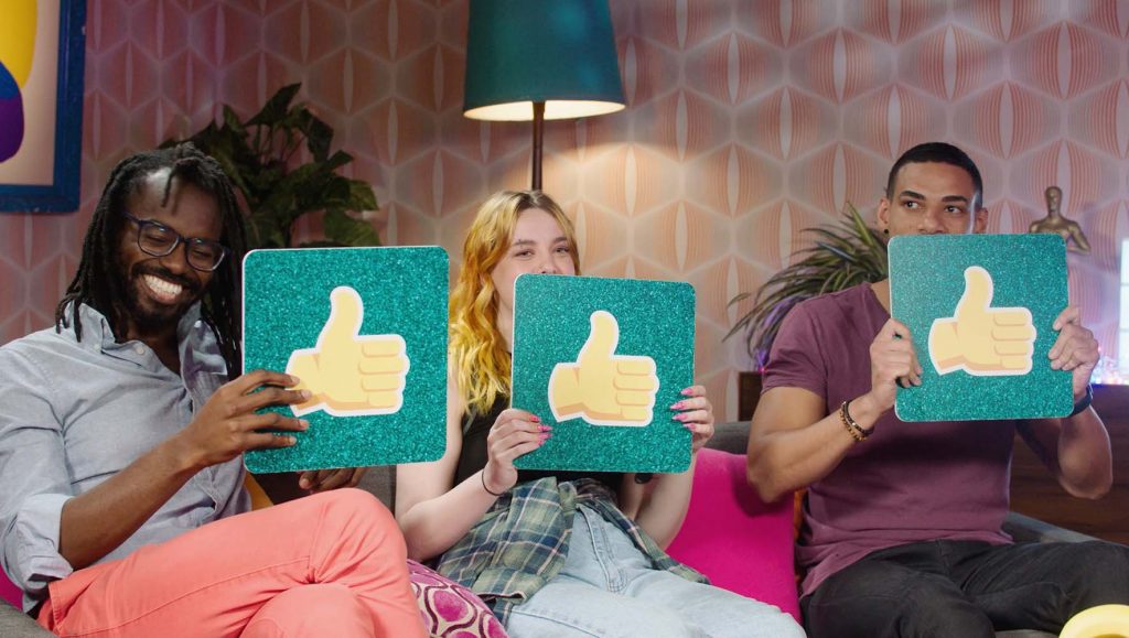 Three people sitting on a lounge, each holding a thumbs up sign